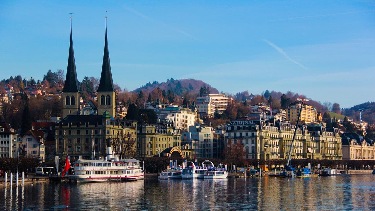Uferpromenade von Luzern am Vierwaldstättersee mit Ausflugsschiffen und der Hofkirche St. Leodegar mit ihren zwei Türmen im Hintergrund.