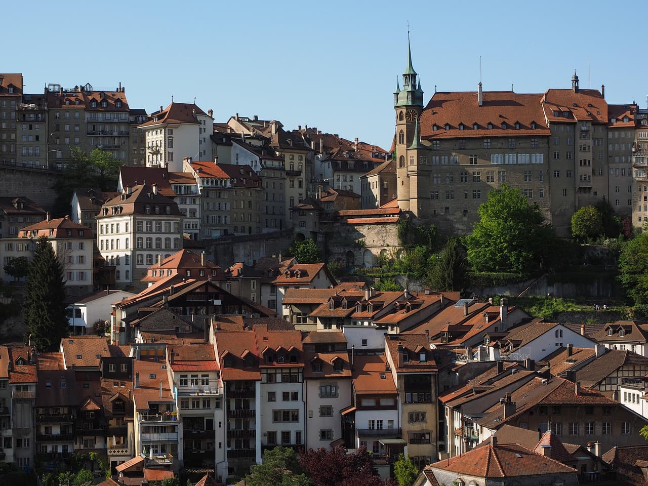 Historische Altstadt von Fribourg in der Schweiz mit dicht stehenden Häusern und der Kathedrale St. Nikolaus auf einem Hügel.
