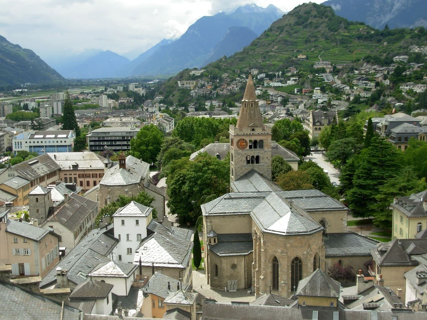 Stadt im Schweizer Kanton Wallis mit historischer Kirche im Zentrum, umgeben von Häusern und Bergen der Alpen.